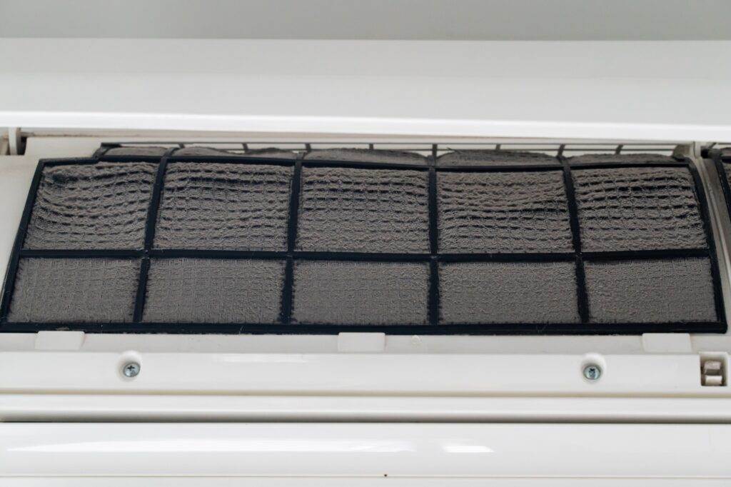 Close-up of an air conditioner filter covered in dust and dirt, indicating it needs cleaning or replacement for proper air conditioning function or to avoid the need for AC repair.