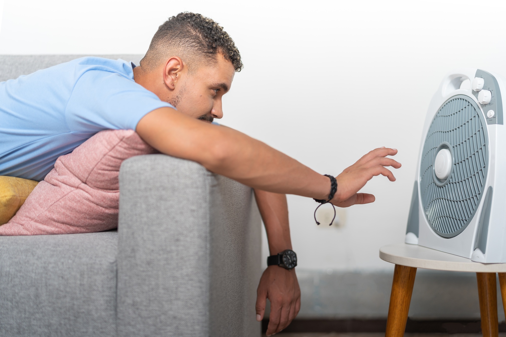 Young man in heat, in front of the fan resting on the sofa